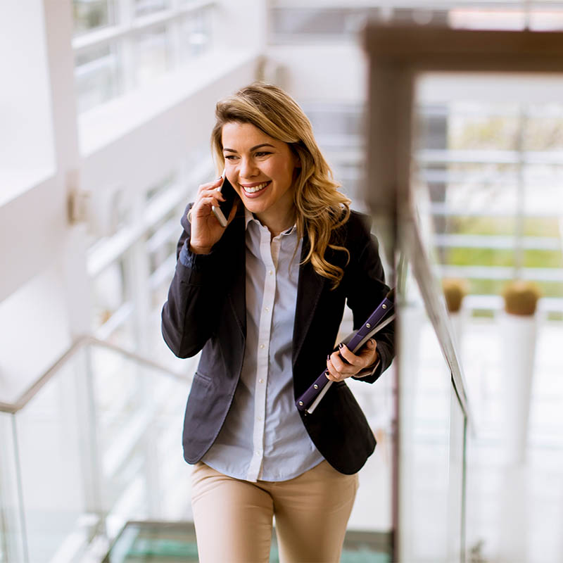 Young businesswoman climbs upstairs in a business building and u ortrait of young businesswoman climbs upstairs in a business building and uses a cell phone