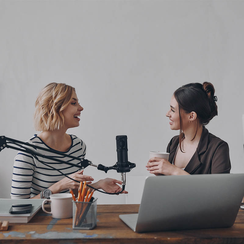Two happy young women communicating while providing live stream in studio together Two happy young women communicating while providing live stream in studio together